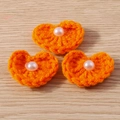 Detail of three handmade orange crochet heart charms with pearls on wood background - Heart Shape / Orange Heart