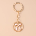 Detailaufnahme des goldenen Schlüsselanhängers mit einem rosa Emaille-Schleifenanhänger im Rahmen - Kreis Schleife