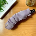 Eleganter lilafarbener Bananen-Haarclip aus Seidenfalten auf einem Holztisch-Hintergrund - Violetter Stoff
