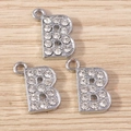 Macro detail of three silver rhinestone letter B charms on a light wood background - Letter B