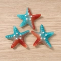 Macro detail of three starfish pendants with blue and orange gradient resin finish - Dark Red