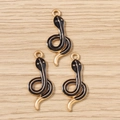 Detailed macro view of three gold-plated snake charms with black enamel on wood background - Black