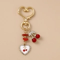 Detalle del llavero de corazón dorado con cerezas rojas y colgante de esmalte blanco - Cereza Corazón