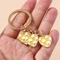 Detail of checkered heart keychains with gold plating held against a soft pink background - Yellow