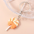 Close-up of spiral orange and yellow lollipop keychain with a bow on soft pink background - Orange