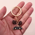 Detail of Halloween keychain with black bat and red fangs charms in hand view - Black Bat