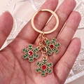 Golden Christmas snowflake keychain with green enamel and red rhinestones held by hand - Gold Snowflake