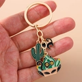 Close-up of golden keychain featuring cute enamel cactus and black cat silhouette charms - Green Cactus Black Cat Style (1453xiaomao)