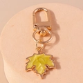 Vue détaillée d'un porte-clés feuille d'érable dorée avec émail jaune sur support en pierre - Jaune
