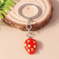 Realistic strawberry keychain with glossy red finish and silver ring on rustic wood - Green Dragon Fruit