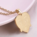 Macro detail of a heart-shaped gold pendant necklace with an engraved abstract face design - Necklace / Gold