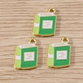 Three book-shaped alloy pendants with green and white enamel on a light wood background - 10 Pieces Pack / Green