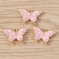 Drei rosa Emaille-Schmetterlingsanhänger mit Goldrahmen auf Holz für DIY-Schmuckherstellung - Rosa
