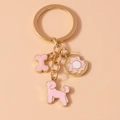 Dettaglio di un portachiavi dorato con ciondoli rosa a forma di osso, barboncino e ciambella - Rosa