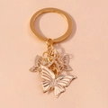 Detail of golden butterfly keychain featuring solid textured and hollow wing pendants - Gold