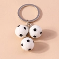Dettaglio portachiavi argento con tre mini ciondoli da calcio 3D su superficie opaca - Calcio