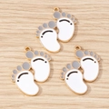 Close-up of three enamel baby footprint charms with gold trim for DIY jewelry making - 10 Pieces Pack / White
