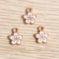 Drei Kirschblüten-Emaille-Anhänger in Roségold-Optik auf hellem Holzgrund - Weiß