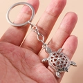 Detailed close-up of a vintage silver metal turtle keychain with openwork coin pattern - Turtle