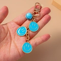 Detail van blauwe emaille smiley-hangers en gouden bel aan een luxe sleutelhanger - Blauw