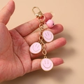 Dettaglio di ciondoli a forma di faccina rosa e campanellino su un portachiavi placcato oro - Rosa