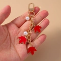 Detail of red maple leaf keychain with white pearls held by hand on beige backdrop - Red