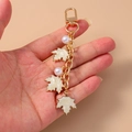Detailed close-up of golden maple leaf keychain with white pearls and enamel charms - White