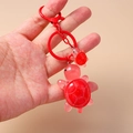 Cute red translucent turtle keychain pendant set with gold-tone ring held in hand - Red