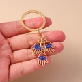 Detailansicht goldener Hamsa-Hand-Schlüsselanhänger mit blauen Evil Eye-Anhängern - Auge Hamsa