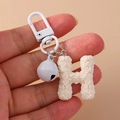Close-up of white rose petal texture on letter H keychain with a small bell - White (H)