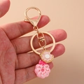 Süßer rosa Donut-Schlüsselanhänger mit Goldverschluss handgehalten vor beigem Hintergrund - Donut