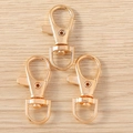 Close-up of three gold-plated star-shaped lobster clasps on a light wood surface - Lobster Clasp (Gold)