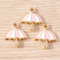 Close-up of pink and white enamel umbrella charms with golden edges on wood - Pink