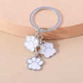 Detail van een zilveren sleutelhanger met drie witte emaille pootjes op een beige voet - Wit