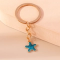Llavero de estrella de mar azul con anillo de metal dorado en soporte rosa suave - Estrella de mar
