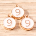 Close-up of circular number 9 charms with gold plating and white enamel on a wooden surface - 10 Pieces Pack / White Number 9 (YD1814baise9)