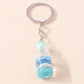 Detalle de un llavero de botella oceánica creativa con conchas pequeñas y arena azul - Concha Azul