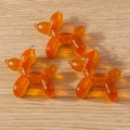 Close-up of three orange translucent balloon dog charms with glitter on wooden surface - Balloon Dog Shape (With Glitter) / 10 Pieces Pack / Brown