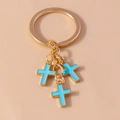 Detail view of gold alloy keychain with three sky blue enamel cross pendants on light background - Blue