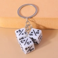 Close-up of three white dice keychains with black math symbols on a warm orange background - White