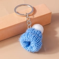 Detail of blue knitted mini hat keychain with white fuzzy pompom on a metal ring - Blue