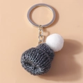 Detailed view of the dark grey knitted mini hat keychain with a white fluffy pom pom - Gray