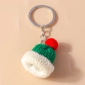 Close-up of handmade green knitted hat keychain with red pompom and silver ring - Green
