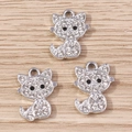 Three silver-plated cat charms with white rhinestones on wooden background - Silver