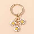 Detailed macro view of small daisy keychain charms with white enamel and golden plating - White