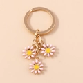 Close-up of golden keychain with three delicate pink daisy flower charms and yellow centers - Pink