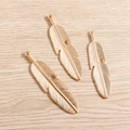 Dettaglio di tre ciondoli a piuma in lega dorata con venature su fondo di legno - Design a Piuma / Oro