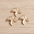 Three vintage gold leaf-shaped metal pendants with clear veins on light wood background - Gold