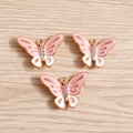Dettaglio di tre ciondoli a farfalla rosa e bianchi con cornice dorata e piccoli strass - Smalto Rosa e Bianco (YD002fense)