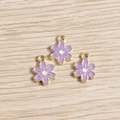 Detail von drei lila Blumenanhängern mit Goldrand auf hellem Holzgrund für DIY-Schmuck - Lila